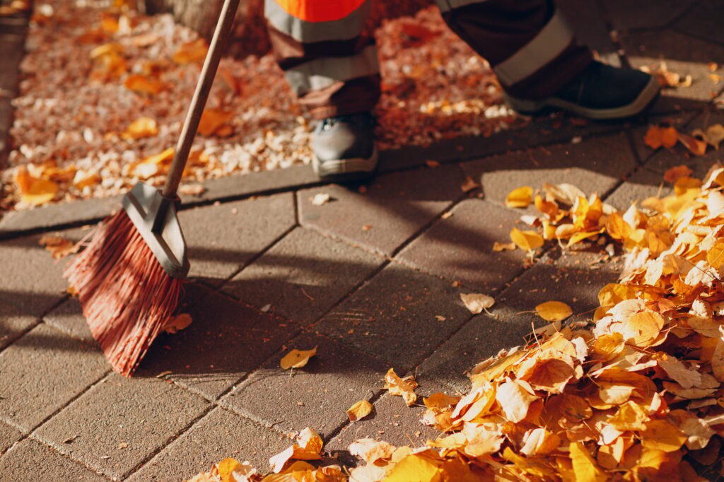 Janitor cleaner sweeping autumn leaves on the street.